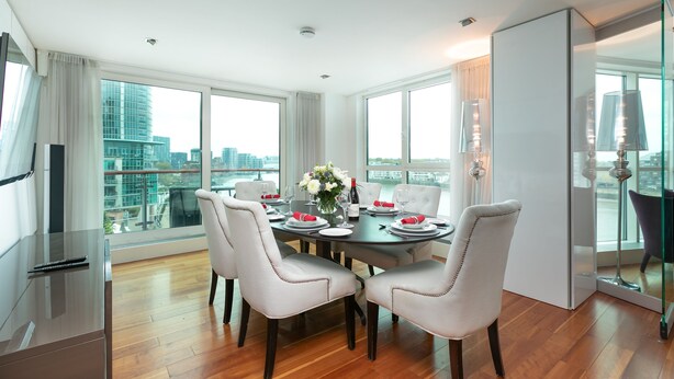 A modern dining room with a large table set for four, large windows offering a city view, and a minimalist decor. - River view Luxury 3bed flat with views (London)
