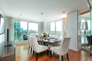 A modern dining room with a large table set for four, large windows offering a city view, and a minimalist decor. - River view Luxury 3bed flat with views (London)