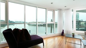 A modern living room with large windows overlooking a river and cityscape. - River view Luxury 3bed flat with views (London)