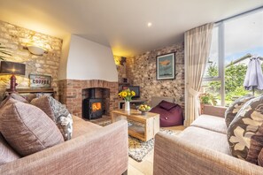A cozy living room with a fireplace, comfortable seating, and a large window with curtains.