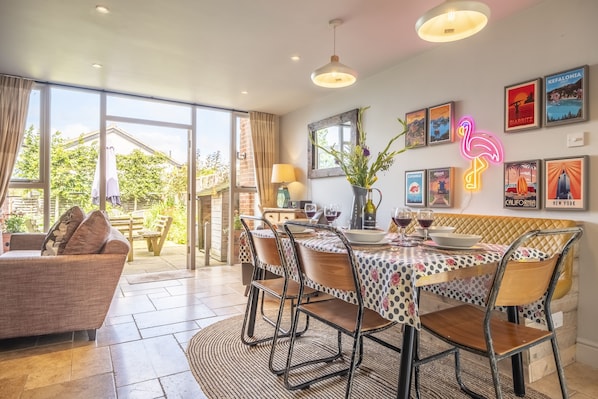 A dining area with a table set for two, surrounded by chairs, a vase with flowers, and framed pictures on the wall.