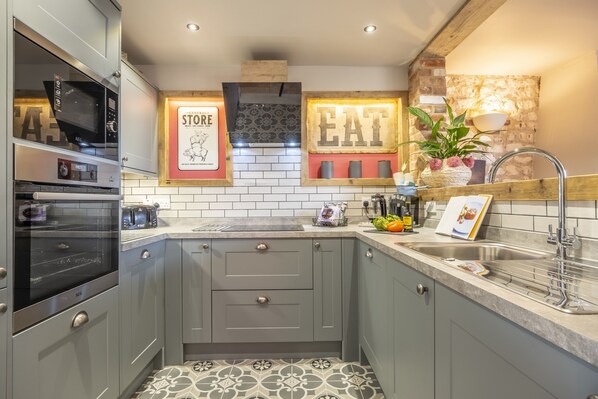 A modern kitchen with grey cabinets, a built-in oven, a microwave, a toaster, and a sink with a wooden countertop. - Cog Cottage, Great Walsingham. Norfolk (Great Walsingham)