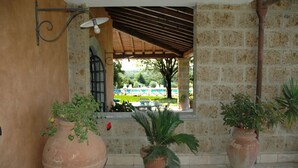 Ein Terrassenbereich im Freien mit großen Terrakottatöpfen, einer Pergola und Blick auf Pool und Garten.
