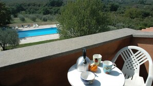 Ein Balkon mit Blick auf einen Swimmingpool, einem Tisch mit Tassen und einem Wasserkocher, sowie ein Stuhl.