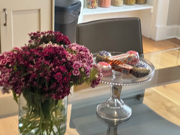 A table with a vase of flowers and a glass cake stand with pastries. - Chic Edinburgh City Centre Apart. close to Castle (Edinburgh)