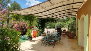 Un patio exterior con zona de comedor cubierta, una parrilla y un pequeño espacio de juego con un niño.