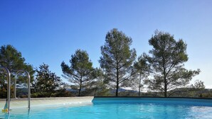 Una piscina con escalera metálica, rodeada de árboles y cielo despejado.
