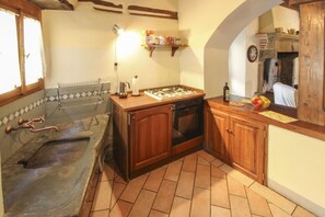 Cozinha equipada com fogão a gás, forno e pia com torneira. Há uma prateleira com potes e um relógio na parede.