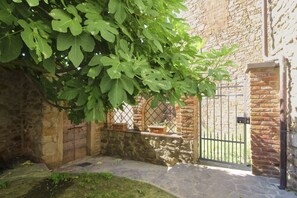 A stone wall with a metal gate, a tree with green leaves, and a brick building in the background. - Ancient stone hamlet in an extremely panoramic position overlooking the wooded Val di Chio. Private (Castiglion Fiorentino)