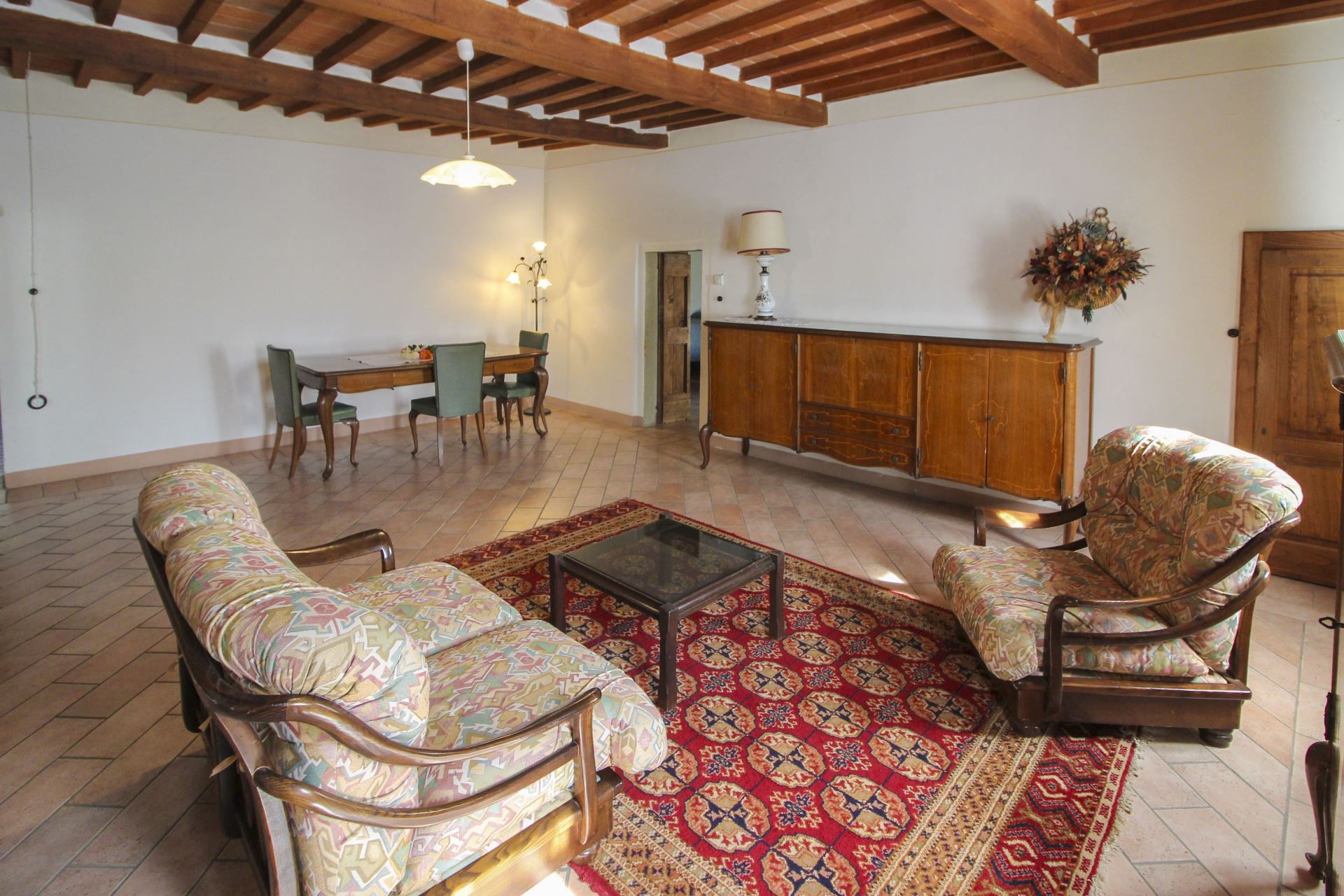 Una sala de estar con techo de madera, una mesa de comedor con sillas, un sofá, un tapete estampado y un aparador.
