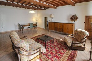 Uma sala de estar com teto de madeira, uma mesa de jantar com cadeiras, um sofá, um tapete estampado e um armário.