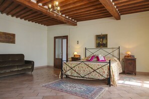 A bedroom with a bed, a wooden ceiling, a nightstand, a lamp, a painting, a sofa, and a door. - Ancient stone hamlet in an extremely panoramic position overlooking the wooded Val di Chio. Private (Castiglion Fiorentino)