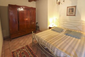 Quarto com cama, guarda-roupa de madeira, mesa de cabeceira com abajur e tapete estampado.