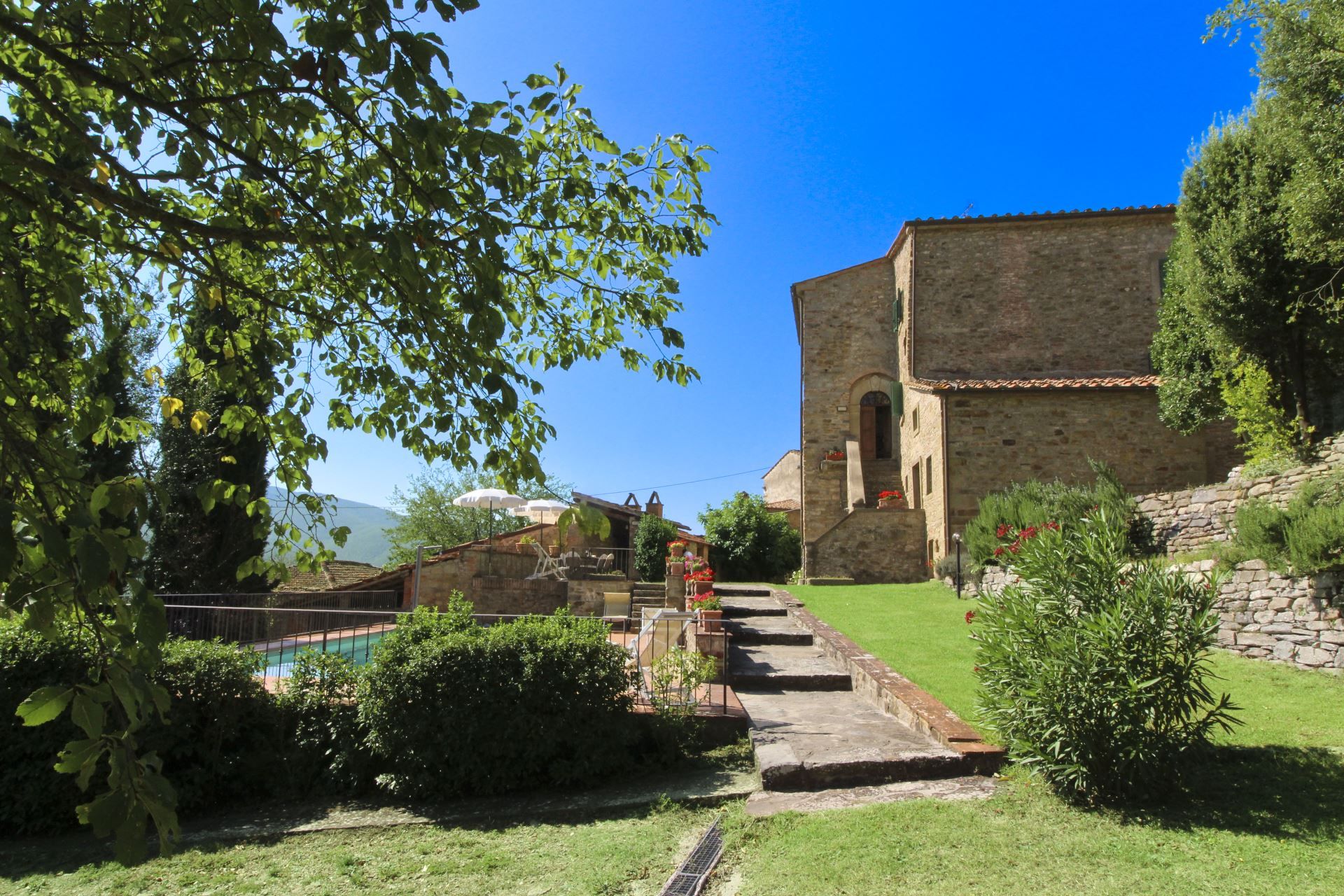 A stone building with a tiled roof, surrounded by greenery and a clear sky.