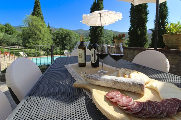 An outdoor dining setup with a table, chairs, a pool, and a scenic view.