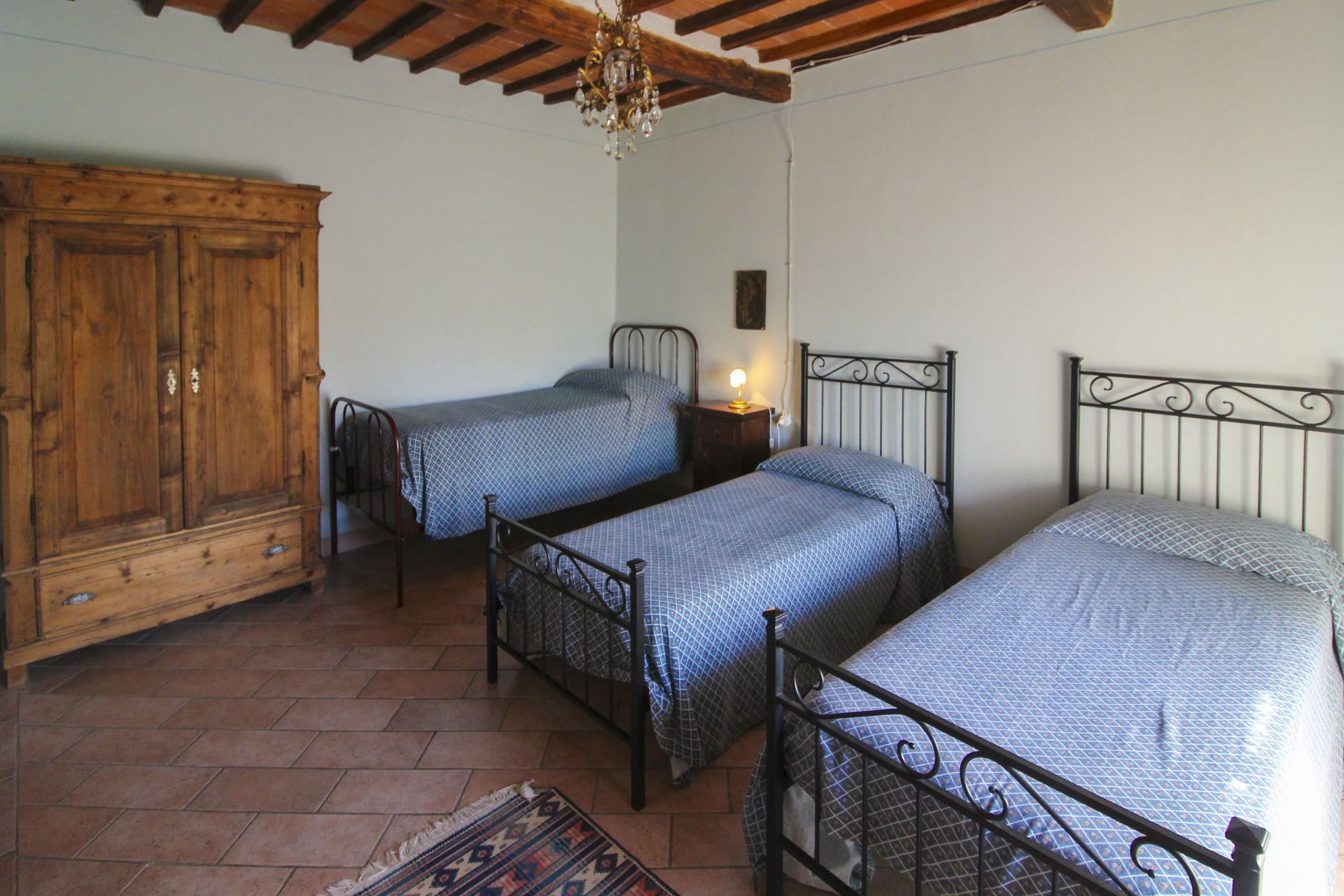 A bedroom with two single beds, a wooden wardrobe, and a chandelier.
