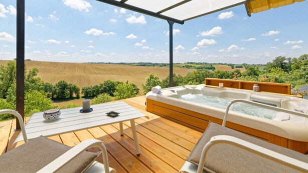 A wooden deck with a hot tub, a table, and chairs, overlooking a rural landscape. - Chambre d'hotes Saga (Savignac-Mona)
