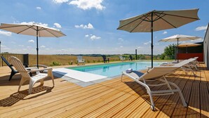 A wooden deck with a pool, lounge chairs, and umbrellas. - Chambre d'hotes Saga (Savignac-Mona)