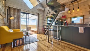 A modern kitchen with a wooden floor, a yellow sofa, and a staircase leading to a loft area. - Chambre d'hotes Saga (Savignac-Mona)