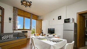 A compact kitchen with a dining area, a sofa, and a television.