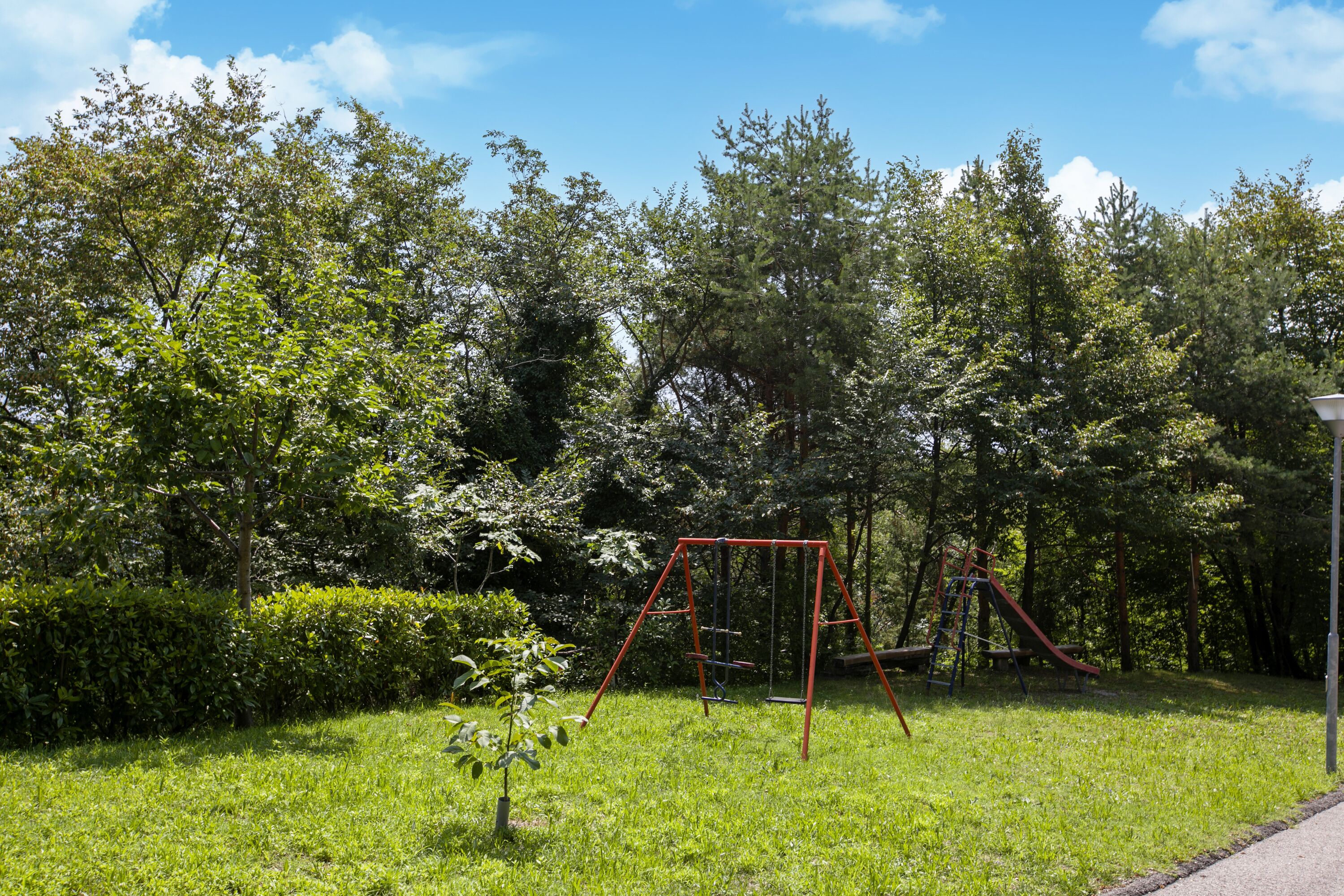 Ein Park mit Schaukel und Rutsche, umgeben von Bäumen und Rasen.