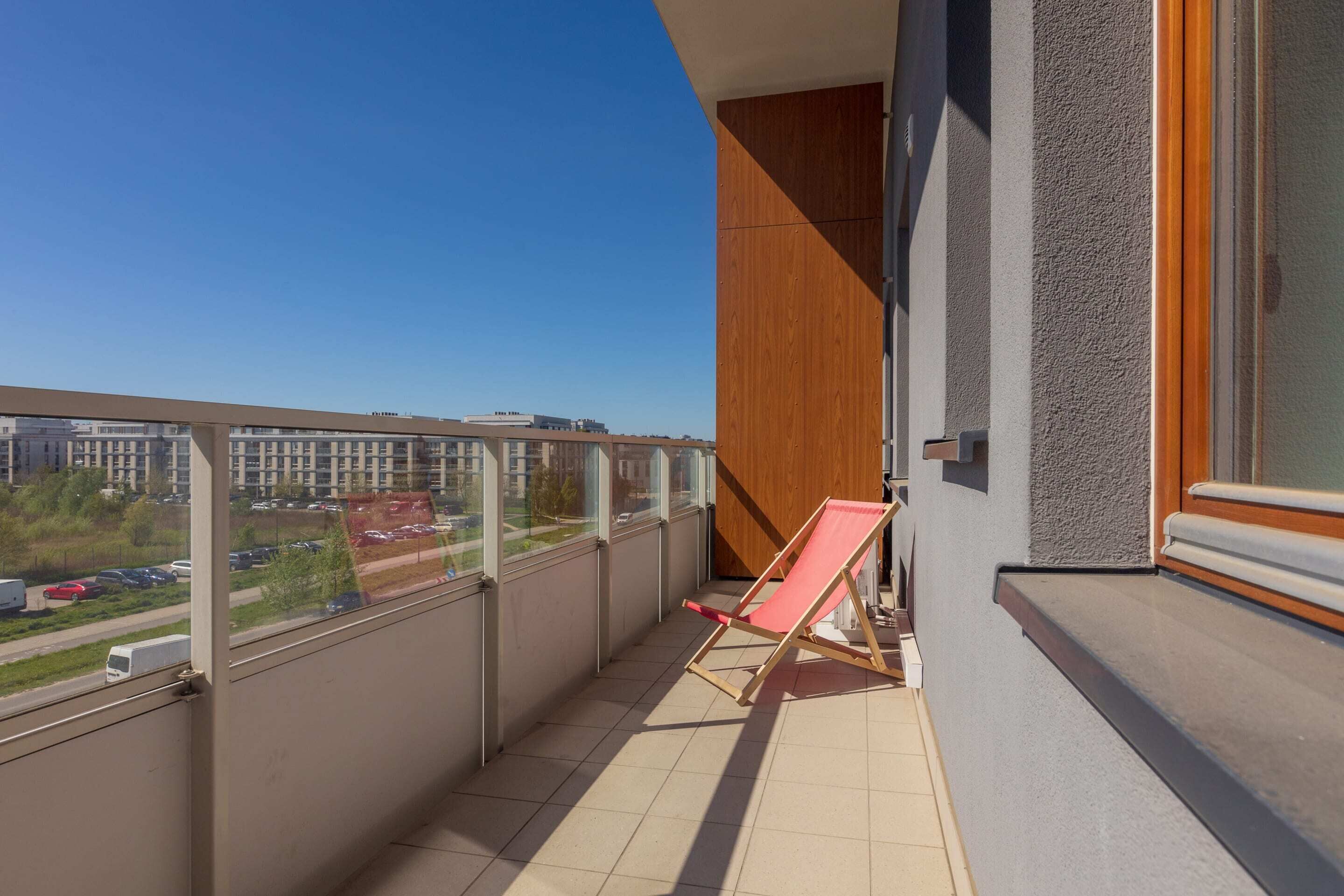 A balcony with a view of a cityscape, a red chair, and a wooden panel on the wall.