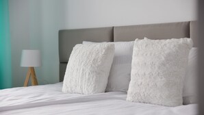 Ein ordentlich bezogenes Bett mit weißer Bettwäsche und zwei gemusterten Kissen.