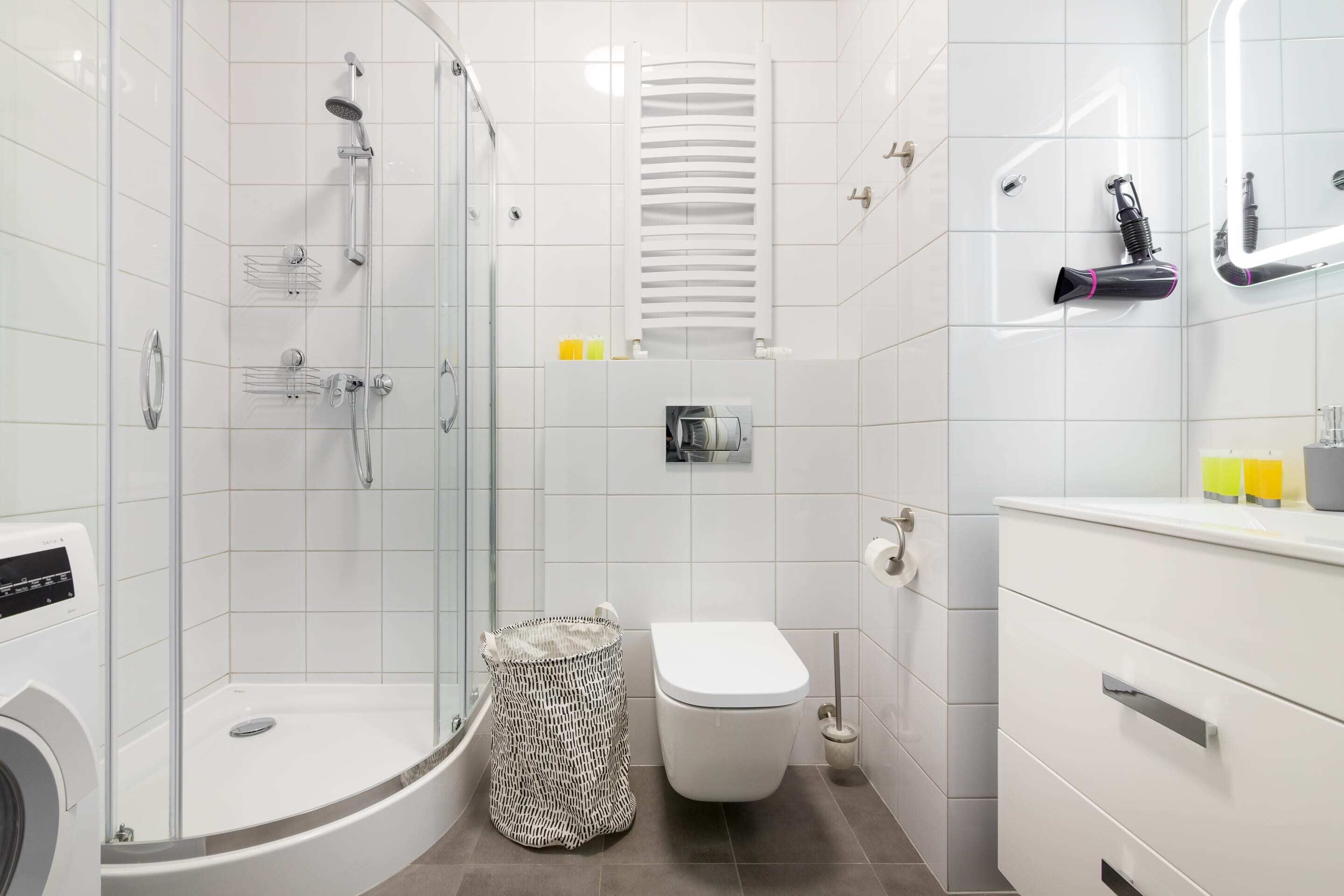 Uma casa de banho moderna com chuveiro em cabine de vidro, sanita e toucador branco com gavetas.