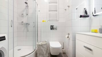 Uma casa de banho moderna com chuveiro em cabine de vidro, sanita e toucador branco com gavetas.