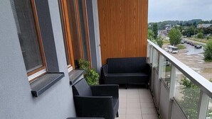 Ein Balkon mit schwarzer Rattanmöbeln, Blumentöpfen und Blick auf einen Fluss sowie entfernte Gebäude.