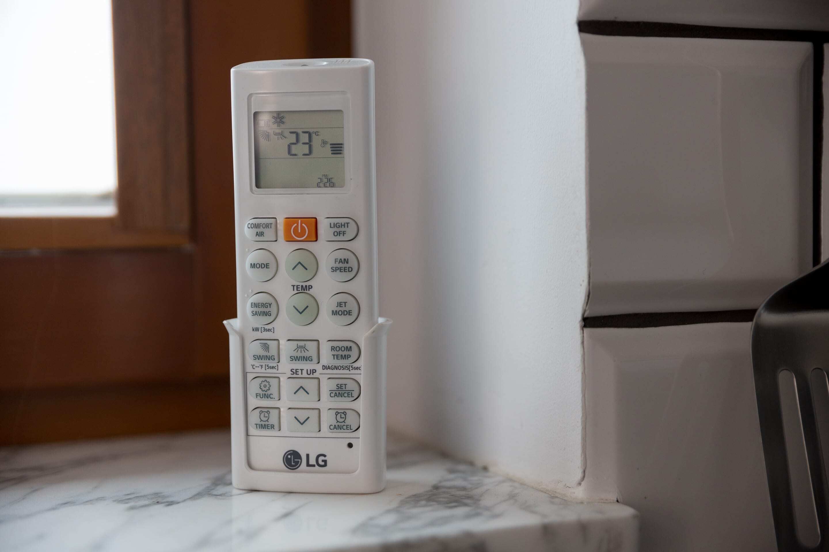 A white LG thermostat on a marble countertop near a window.