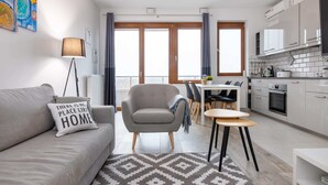 Ein modernes Wohnzimmer mit einer Couch, einem Sessel, einem Esstisch und einer Küchenzeile mit Schränken und Geräten.