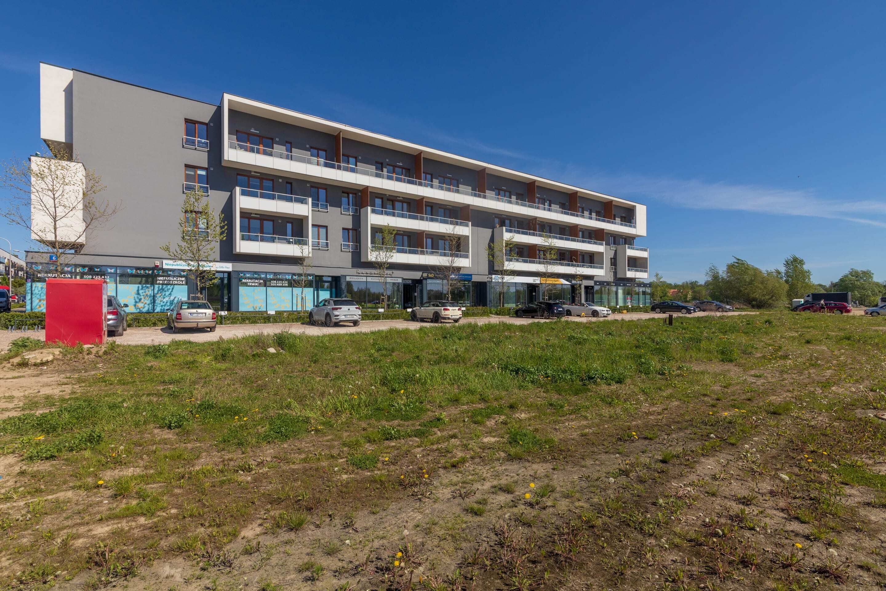 A multi-story building with a flat roof and a large parking area in front.
