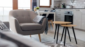 Ein modernes Wohnzimmer mit einer Couch, einem kleinen runden Tisch und einer Küchenzeile mit Schränken und Geräten.