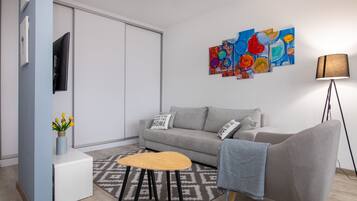 A modern living room with a grey sofa, a wooden coffee table, a patterned rug, a wall-mounted TV, and abstract art.