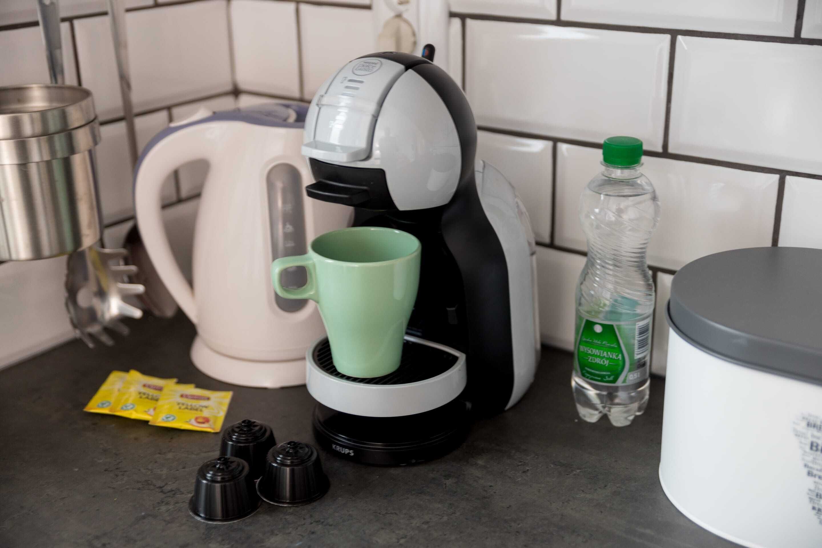 Una encimera de cocina con una cafetera, una taza verde, una botella de agua y algunos condimentos.