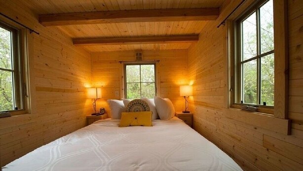 Un dormitorio de cabaña de madera con una cama, dos lámparas de noche y ventanas.