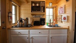 Interior de una cabaña de madera con cocina, que incluye una cafetera, hervidor y microondas en un estante sobre la encimera.