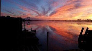 Un lago tranquilo al atardecer, con un muelle y una torre de agua en el fondo.