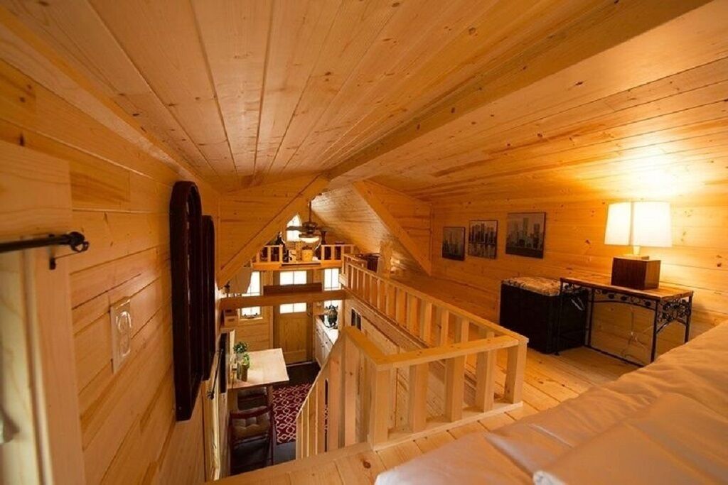 A wooden cabin interior with a staircase, a dining area, and a bed.