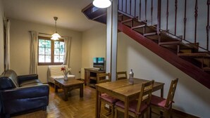 Una sala de estar con sofá, una mesa de comedor con sillas, televisión y una escalera de madera.