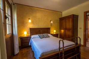 A bedroom with a wooden bed, two bedside tables with lamps, a wardrobe, and a window with curtains.