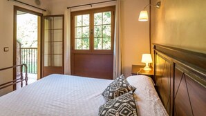 Un dormitorio con una cama, una mesita de noche con lámpara, una ventana con cortinas y vistas al exterior.