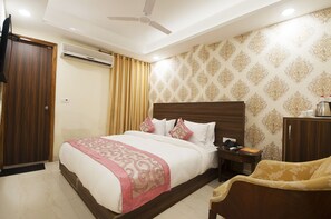 Habitación de hotel con una cama grande, cabecera de madera, mesita de noche, escritorio, silla, armario, equipo de aire acondicionado y ventilador de techo.
