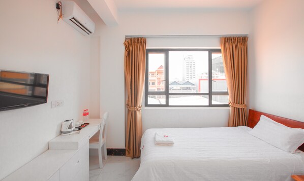 Ein Hotelzimmer mit Bett, Schreibtisch mit Stuhl, Flachbildfernseher und einem Fenster mit Vorhängen.