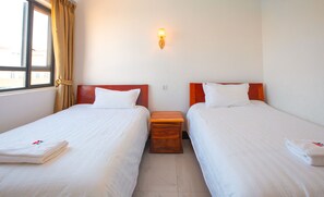 Ein Hotelzimmer mit zwei Einzelbetten, einem Nachttisch, einer Wandleuchte und einem Fenster mit Vorhängen.