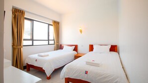 A hotel room with two single beds, a window with curtains, a bedside table, and a wall-mounted light. - Cambodia Eren Hotel (Phnom Penh)