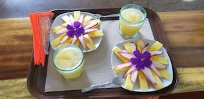 A tray with three fruit cups and a glass of juice, each decorated with a purple flower and slices of fruit.