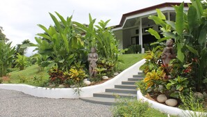 A garden with statues, a curved pathway, and a building with a covered porch. - Villas Octogoña (Ciudad Cortés)