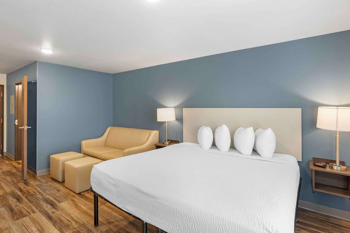 A hotel room with a large bed, a sofa, two nightstands with lamps, and a wooden floor.